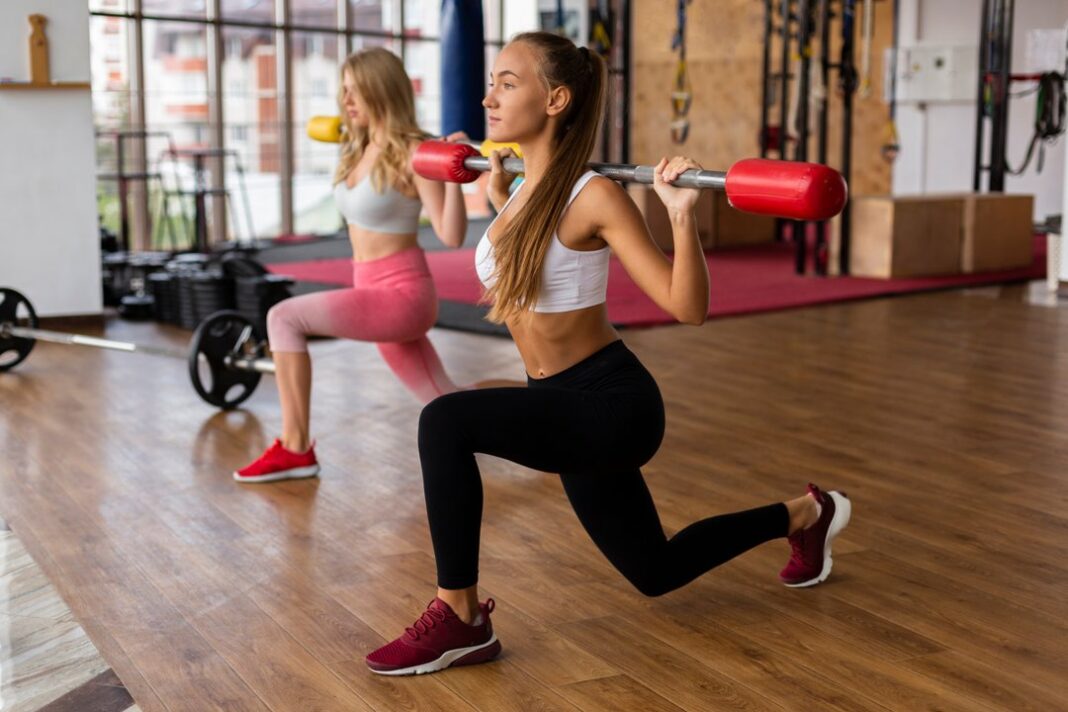 Mujer realizando ejercicio de fuerza con mancuernas en un gimnasio.