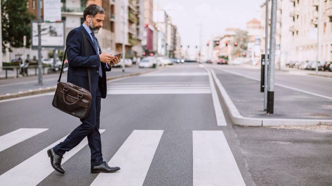 Peatón cruzando la calle mientras mira el celular, con semáforo de fondo en la Ciudad de Buenos Aires
