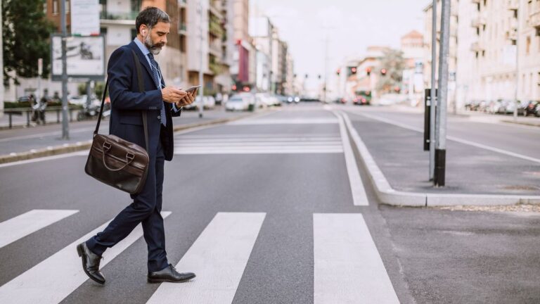 Peatón cruzando la calle mientras mira el celular, con semáforo de fondo en la Ciudad de Buenos Aires