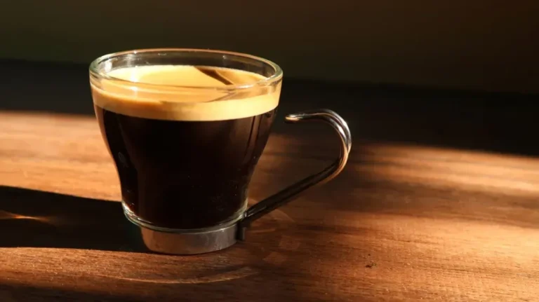 Taza de café recién preparado con granos de café al lado